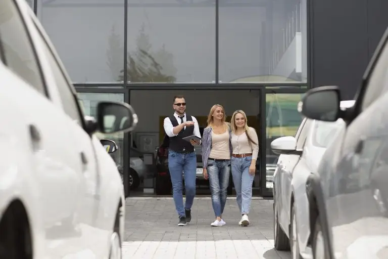 Two smiling customers walk out of a Calgary car dealership with a sales associate, surrounded by parked vehicles.